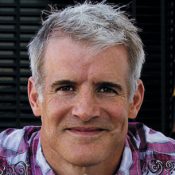 Portrait of a smiling man with short gray hair wearing a purple plaid shirt.